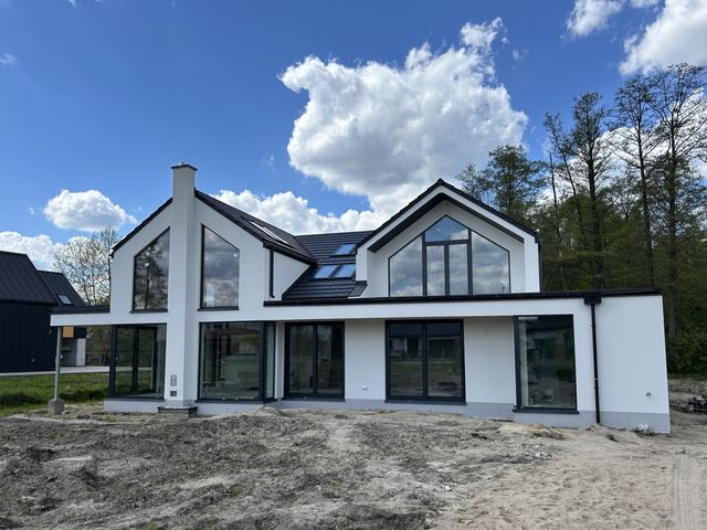 Dokončená moderní vila s bílou omítkou a tmavými okny